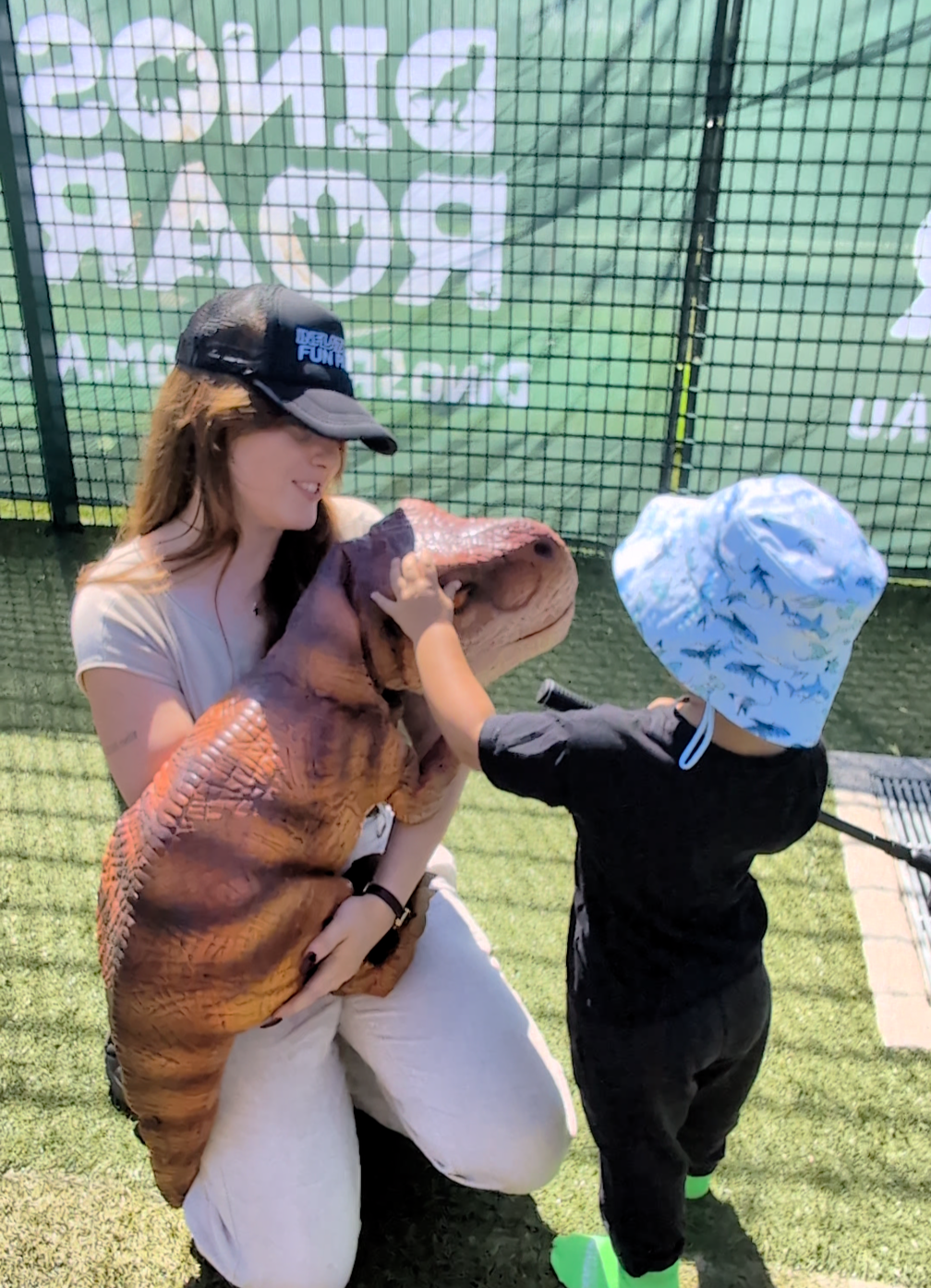 Child touching a baby dinosaur puppet with handler